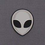 The Alien Gray (Double Layer Silicone) Flexfit® Mesh Trucker Cap by Eternal Glyph features a minimalistic grey alien head icon with black oval eyes on a smooth, light gray background, inspired by classic UFO pop culture.