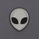The Alien Gray (Double Layer Silicone) Flexfit® Mesh Trucker Cap by Eternal Glyph features a minimalistic grey alien head icon with black oval eyes on a smooth, light gray background, inspired by classic UFO pop culture.