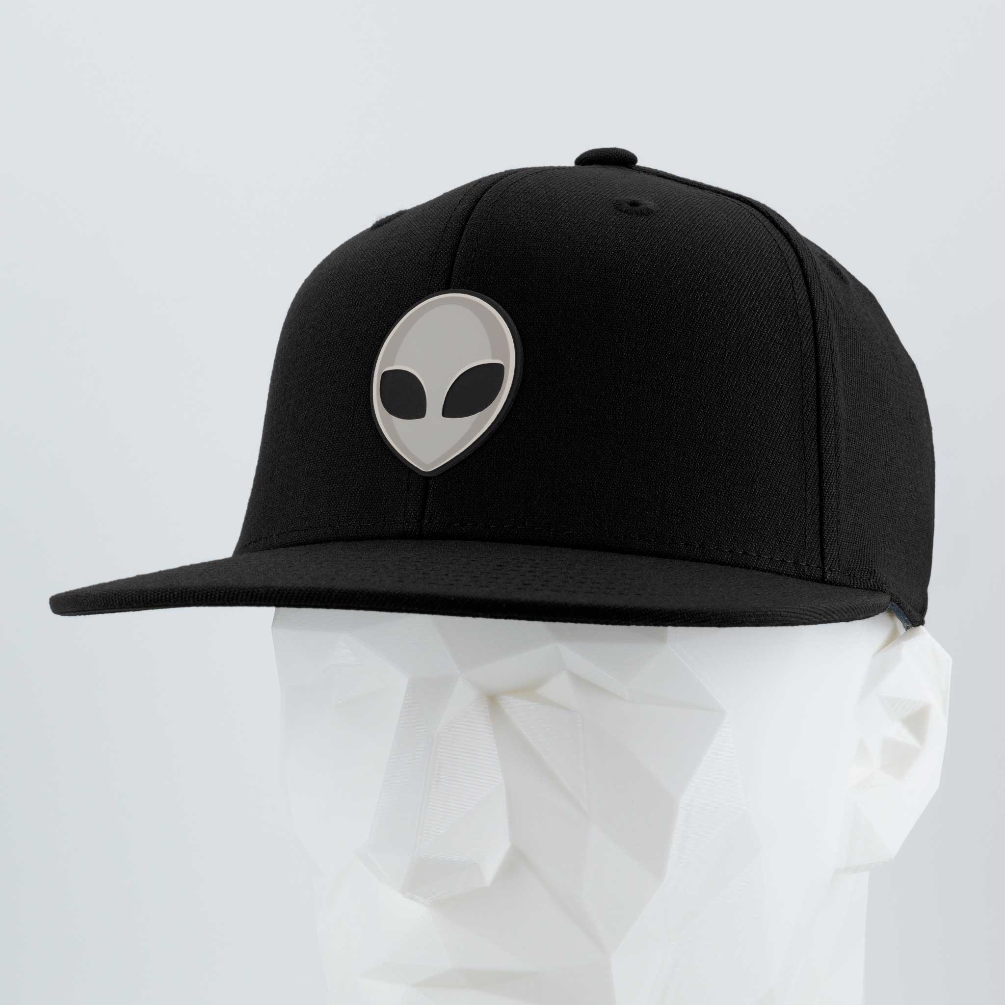 The Eternal Glyph Alien Gray (Double Layer Silicone) Flexfit® Flat Bill Premium Fitted Cap is a black cap with a silver alien glyph logo, inspired by UFO pop culture, shown on a white mannequin against a light gray backdrop.