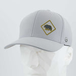 The Eternal Glyph Bear Crossing Sign (Silicone) Flexfit® Cool & Dry Cap is a light gray hat with a yellow bear-crossing patch, shown on a white faceted mannequin head.