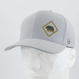 The Eternal Glyph Bear Crossing Sign (Silicone) Flexfit® Cool & Dry Cap is a light gray hat with a yellow bear-crossing patch, shown on a white faceted mannequin head.