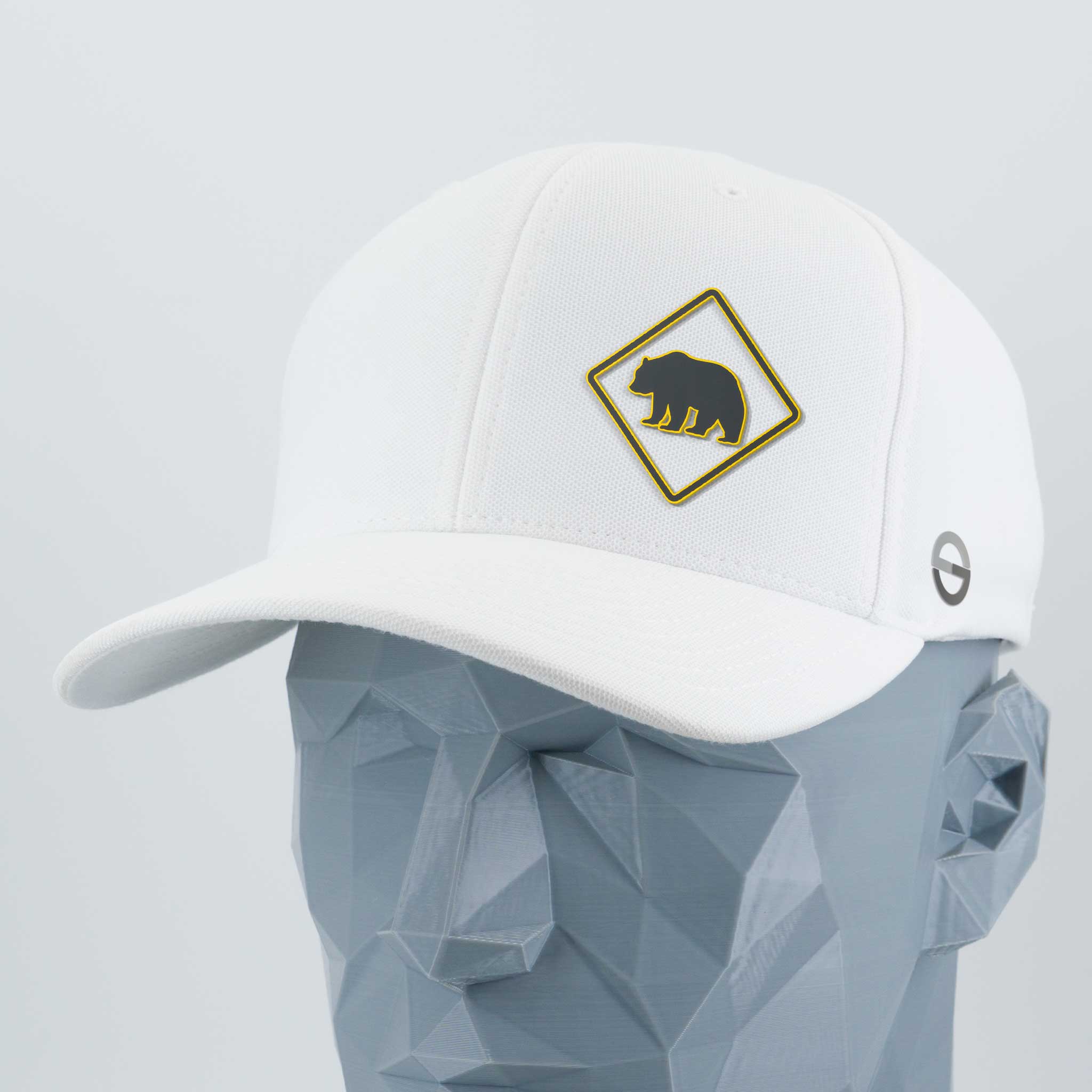The Bear Crossing Sign (Silicone) - Flexfit® Cool & Dry Cap by Eternal Glyph is a white cap with a diamond-shaped black bear patch and a small circular logo, displayed on a gray geometric mannequin head.