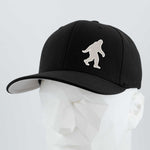 The Eternal Glyph Bigfoot Silhouette Albino Flexfit® Premium Wool Blend Cap features a white Bigfoot design on black and is shown on a geometric mannequin head—ideal for Pacific Northwest folklore fans.