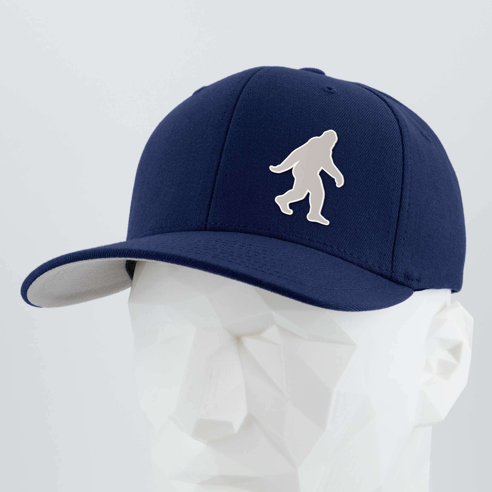 The Eternal Glyph Bigfoot Silhouette Albino (Silicone) Flexfit® Premium Wool Blend Cap features a white Bigfoot on navy blue, inspired by Pacific Northwest folklore, shown on a white geometric mannequin head.