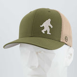 The Eternal Glyph Bigfoot Silhouette Albino (Silicone) Flexfit® Mesh Trucker Cap in green and beige, inspired by Pacific Northwest folklore, features a bold Bigfoot logo and is shown on a faceted white mannequin head.