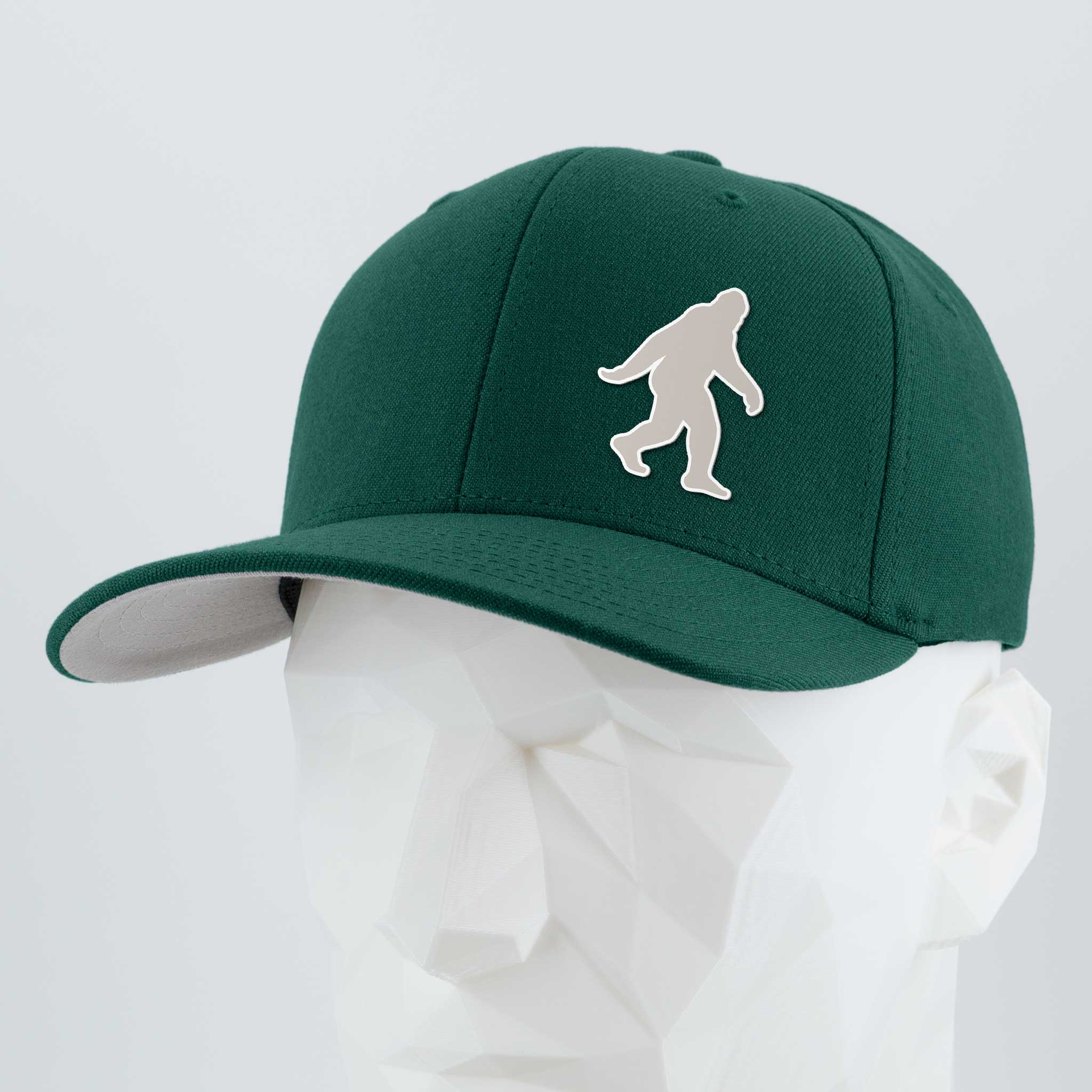 The Eternal Glyph Bigfoot Silhouette Albino Cap, a dark green Flexfit® Premium Wool Blend, features a white Bigfoot silhouette on the front—displayed on a white geometric mannequin head against a plain backdrop.