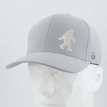 The Eternal Glyph Bigfoot Silhouette Albino (Silicone) Flexfit® Cool & Dry Cap is a light gray cap with a white Bigfoot silhouette, inspired by Pacific Northwest folklore, shown on a white geometric mannequin head.
