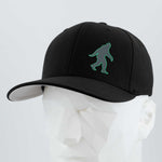 The Eternal Glyph Bigfoot Silhouette (Silicone) Flexfit® Premium Wool Blend Cap in black features a green Bigfoot silhouette on the front, shown on a white mannequin against a plain background—perfect for explorers and adventure seekers.