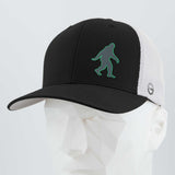 The Eternal Glyph Bigfoot Silhouette (Silicone) Flexfit® Mesh Trucker Cap features a green outlined Bigfoot icon on a black and white cap, shown here on a white geometric mannequin head.