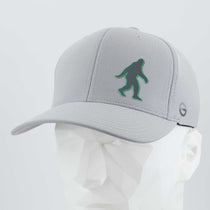 The Eternal Glyph Bigfoot Silhouette (Silicone) Flexfit® Cool & Dry Cap in grey features a vibrant green Bigfoot on the front, making it an ideal adventure accessory for outdoor enthusiasts. Shown here on a white mannequin head.