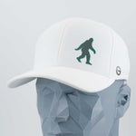 The Eternal Glyph Bigfoot Silhouette (Silicone) Flexfit® Cool & Dry Cap is a white baseball hat with a dark green Bigfoot design, shown on a faceted gray mannequin head—ideal for fans of this legendary wilderness icon.