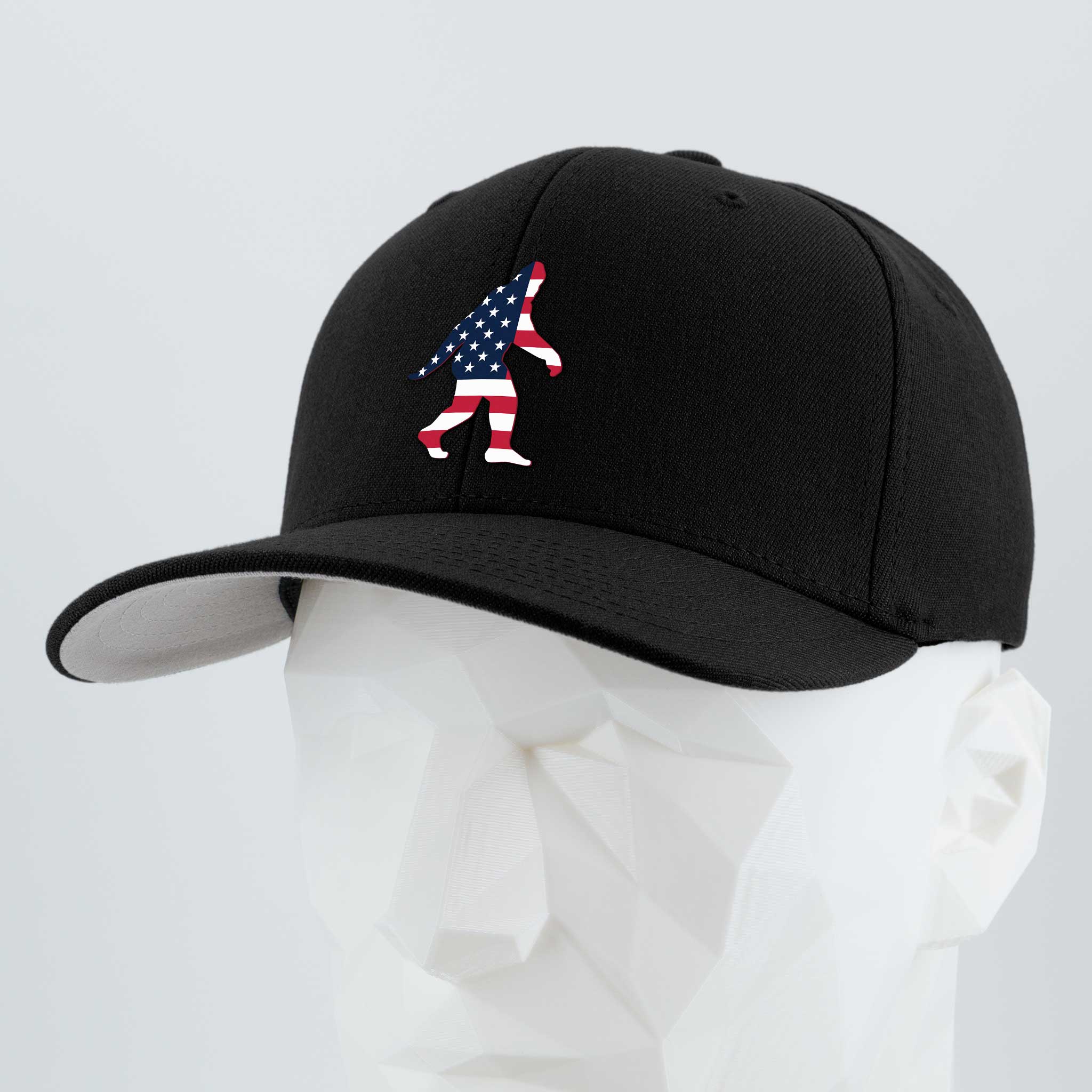 The Eternal Glyph Patriotic Bigfoot (Silicone) Flexfit® Premium Wool Blend Cap is a black hat with an American flag Bigfoot silhouette, shown on a white faceted mannequin—a modern tribute to wilderness folklore.