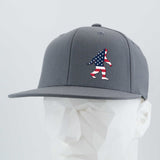 The Eternal Glyph Patriotic Bigfoot (Silicone) Flexfit® Flat Bill Premium Fitted Cap is a gray snapback hat with an American flag Bigfoot silhouette, shown on a white geometric mannequin—a tribute to Sasquatch legends and U.S. pride.