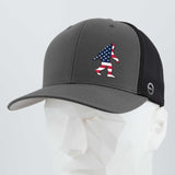 The Eternal Glyph Patriotic Bigfoot (Silicone) Flexfit® Mesh Trucker Cap in dark gray and black features a small American flag Sasquatch silhouette on the front, shown here on a white geometric mannequin head.
