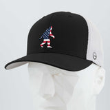 The Eternal Glyph Patriotic Bigfoot (Silicone) Flexfit® Mesh Trucker Cap in Black/White features a bold American flag Bigfoot silhouette, shown on a white faceted mannequin—ideal for wilderness folklore fans.
