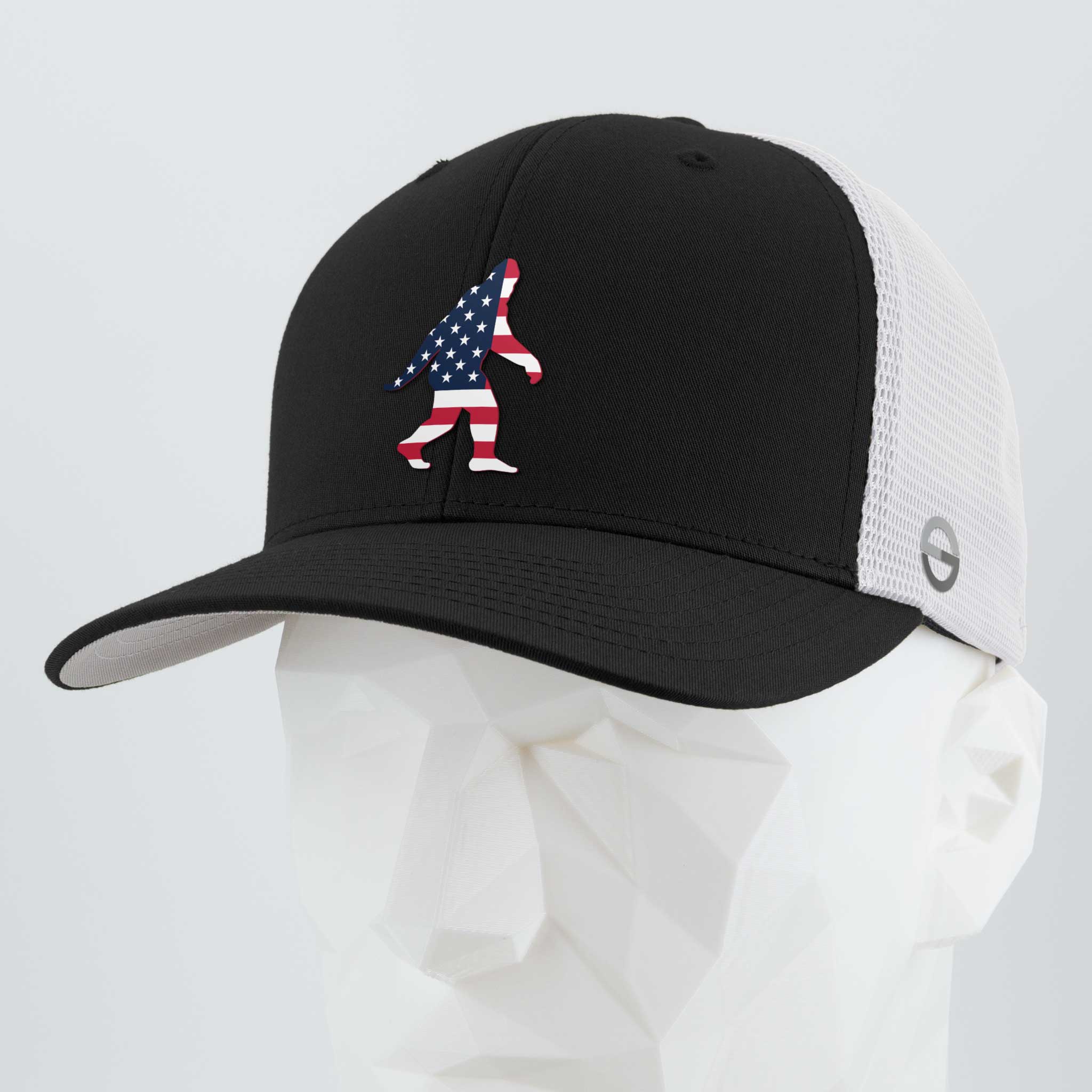 The Eternal Glyph Patriotic Bigfoot (Silicone) Flexfit® Mesh Trucker Cap in Black/White features a bold American flag Bigfoot silhouette, shown on a white faceted mannequin—ideal for wilderness folklore fans.