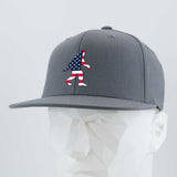 The Eternal Glyph Patriotic Bigfoot (Silicone) Flexfit® Flat Bill Premium Fitted Cap showcases an American flag Bigfoot silhouette on gray—ideal for wilderness folklore fans. Displayed on a faceted white mannequin.