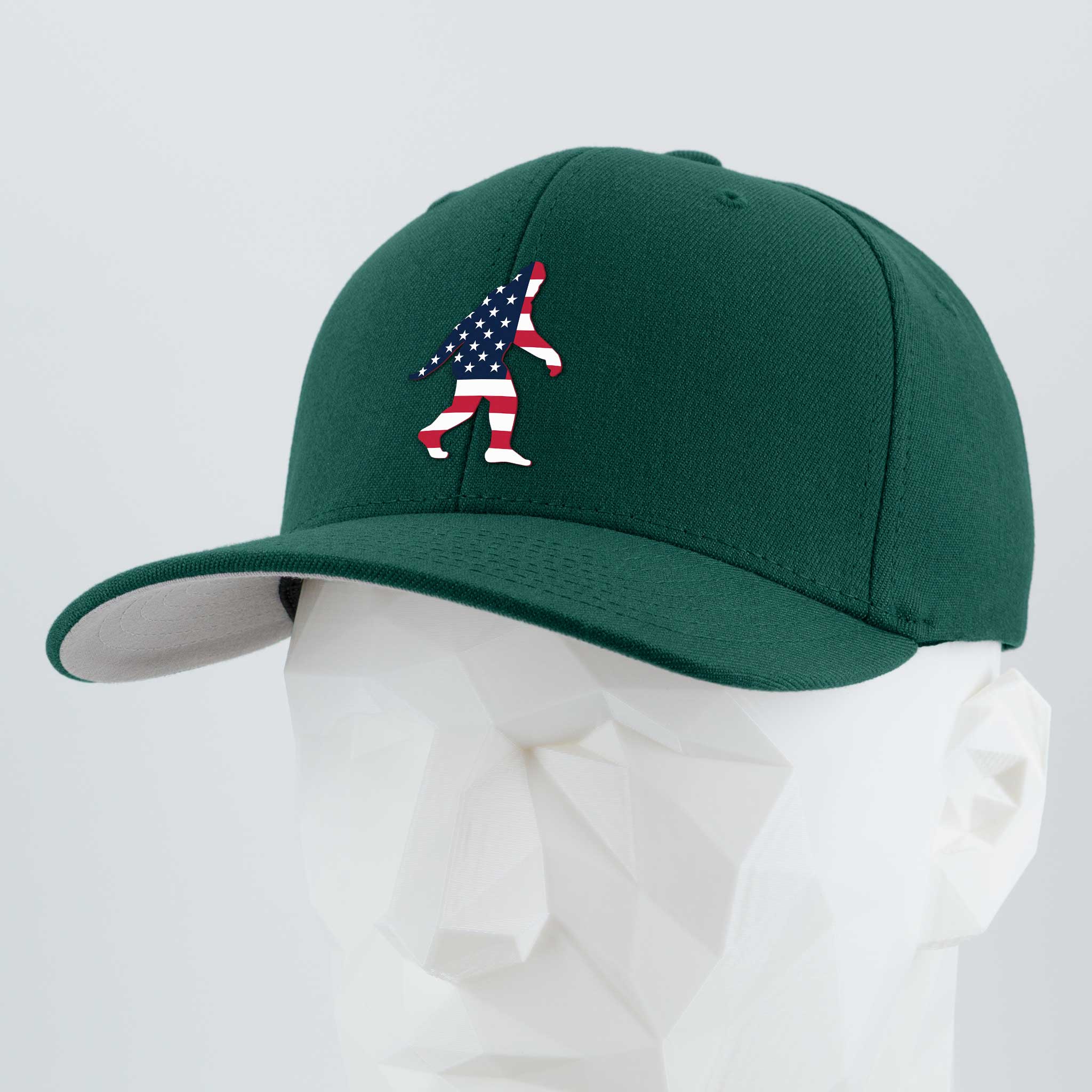 The Eternal Glyph Patriotic Bigfoot (Silicone) Flexfit® Premium Wool Blend Cap, in dark green, features a silicone American flag-patterned Bigfoot silhouette and is shown on a white faceted mannequin head.