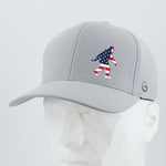 The Eternal Glyph Patriotic Bigfoot (Silicone) Flexfit® Cool & Dry Cap is a light gray baseball cap with an American flag-themed Bigfoot design, shown on a white geometric mannequin. Ideal for wilderness folklore fans.