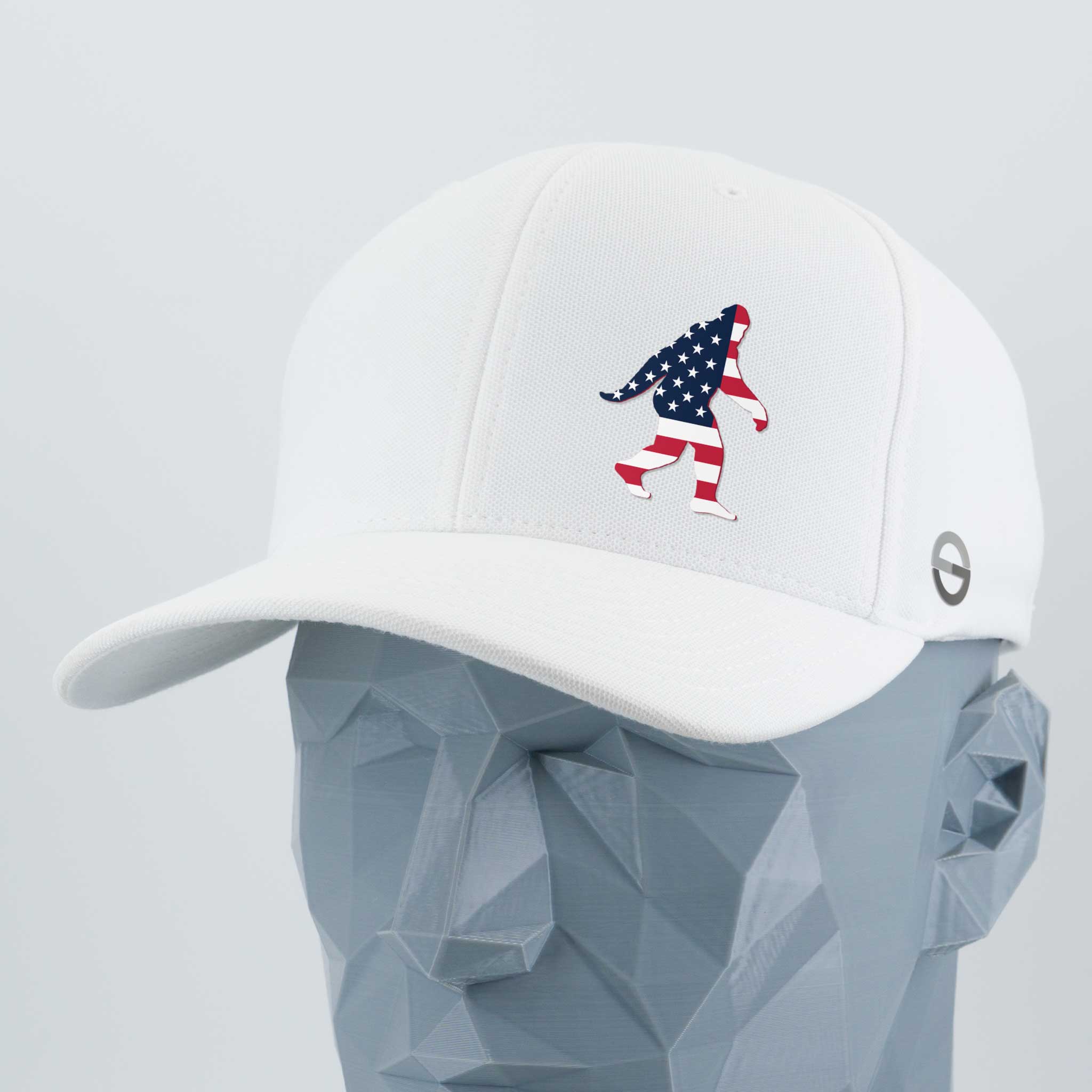 The Eternal Glyph Patriotic Bigfoot (Silicone) Flexfit® Cool & Dry Cap features a white design with an American flag Bigfoot on the front and a side logo—ideal for wilderness folklore fans. Displayed on a faceted gray mannequin head.