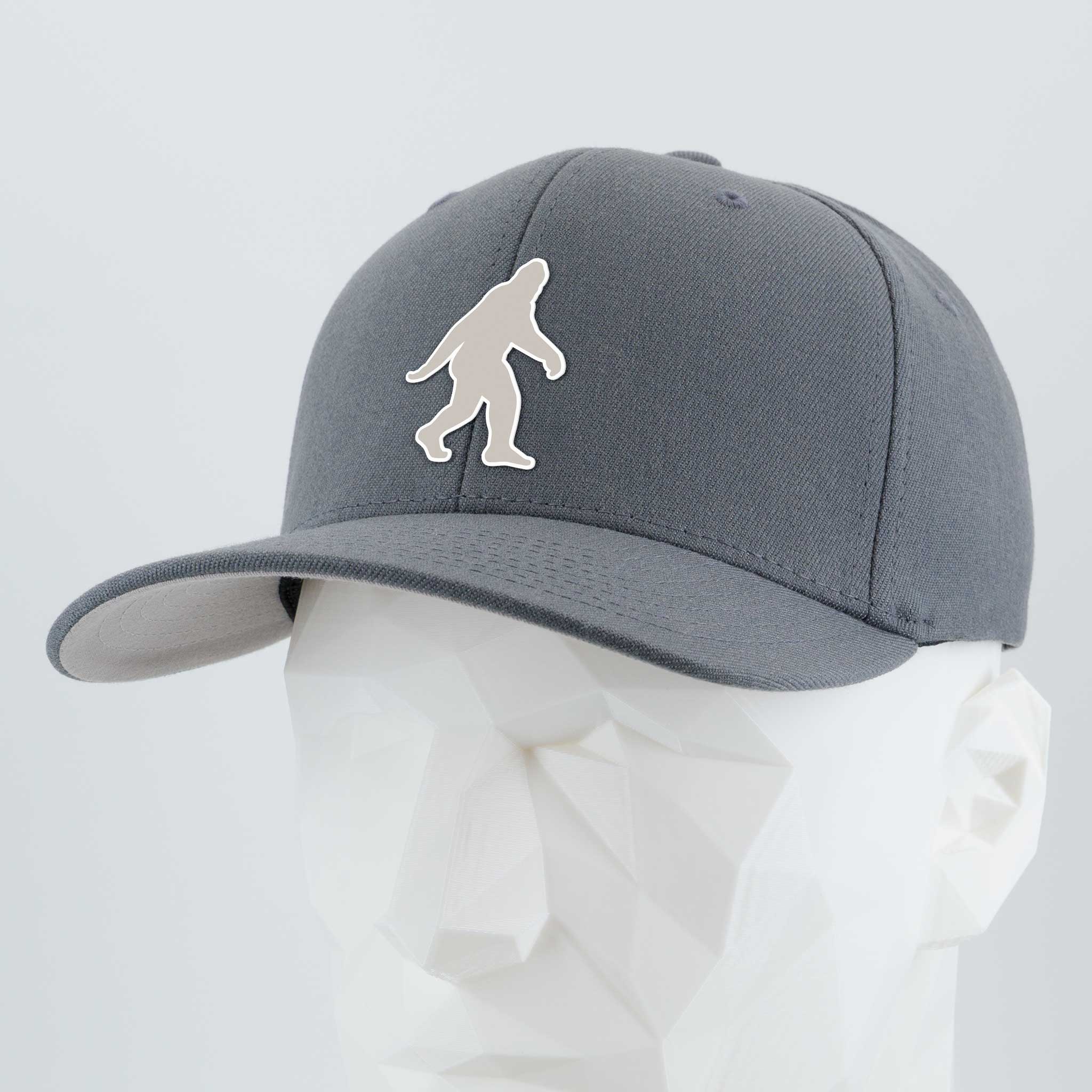 The Eternal Glyph Bigfoot Silhouette Albino Flexfit® Premium Wool Blend Cap in dark gray, featuring a bold Bigfoot design inspired by Pacific Northwest folklore, is shown on a faceted white mannequin head against a plain light background.