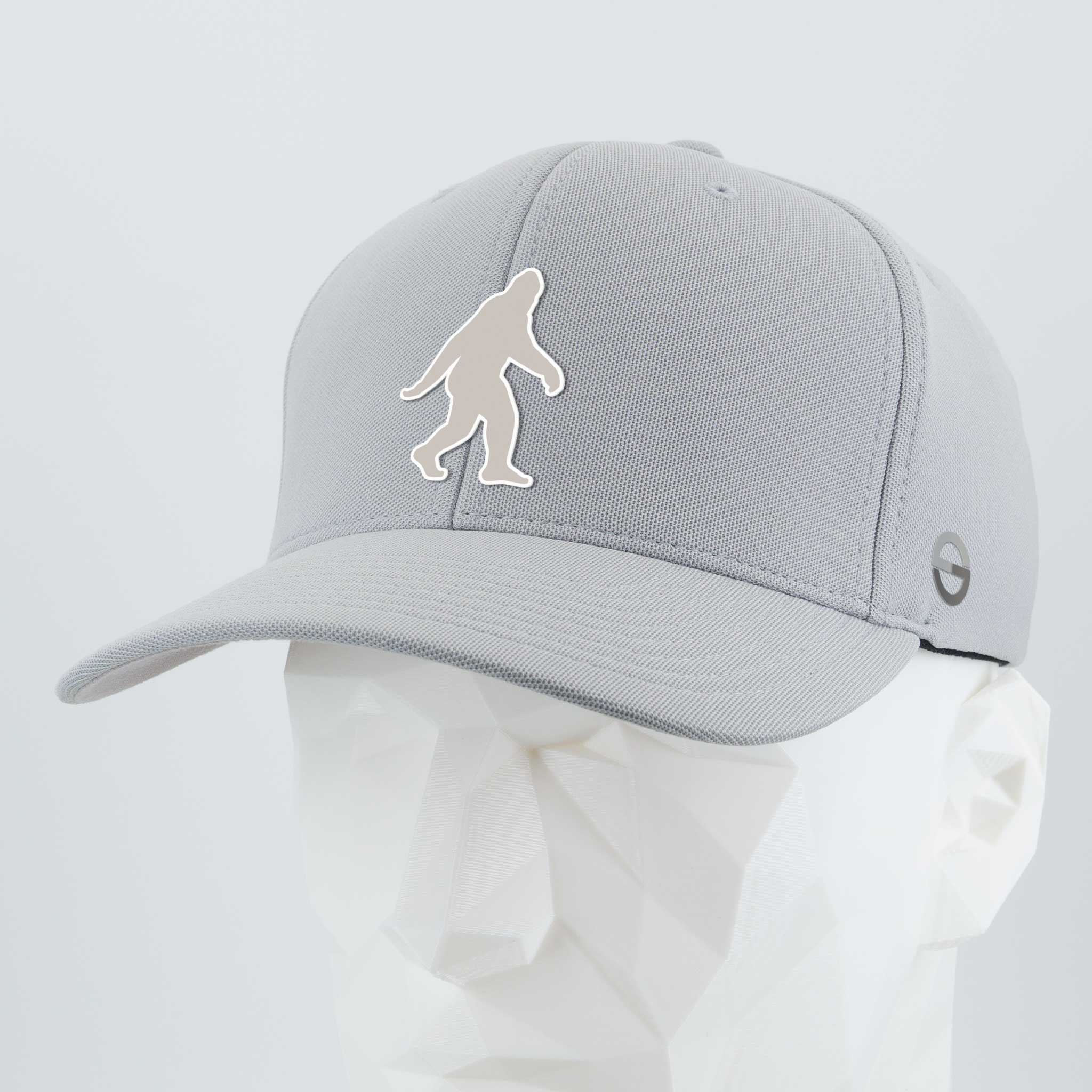 The Eternal Glyph Bigfoot Silhouette Albino Flexfit® Cool & Dry Cap in silver features a bold Bigfoot design on the front and a small folklore-inspired circular logo on the side, displayed on a faceted white mannequin head.