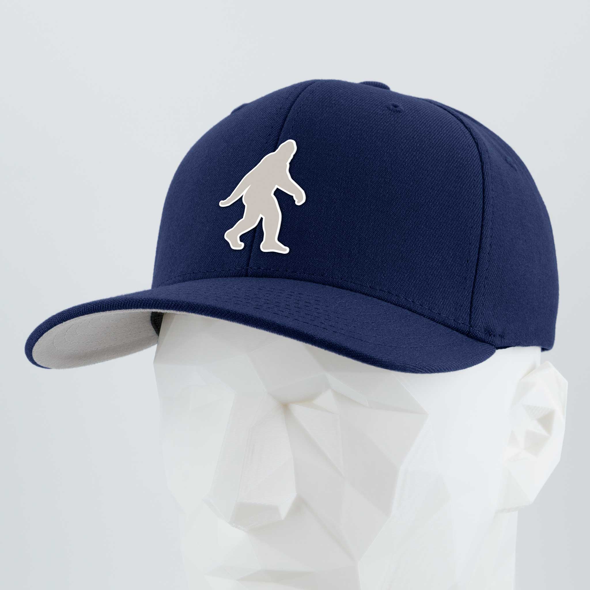 The Eternal Glyph Bigfoot Silhouette Albino (Silicone) Flexfit® Premium Wool Blend Cap in navy features a white Bigfoot design, inspired by Pacific Northwest folklore, shown on a white geometric mannequin head against a light gray backdrop.