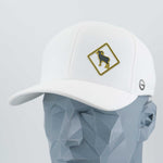 A geometric gray mannequin head displays the Eternal Glyph Bighorn Sheep Crossing Sign (Silicone) Flexfit® Cool & Dry Cap—white, with a yellow-bordered patch showing a black bighorn sheep silhouette and a small gray circular side logo.