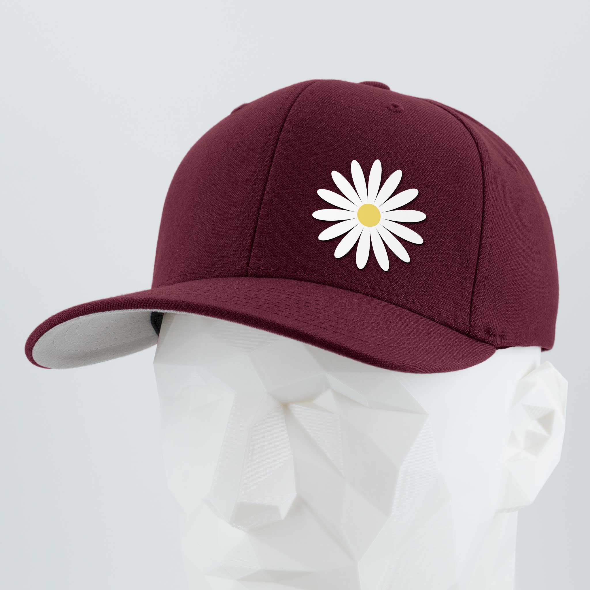 The Daisy (Silicone) - Flexfit® Premium Wool Blend Cap by Eternal Glyph features a maroon design with a white daisy and yellow center, shown on a white geometric mannequin against a light gray background—a symbol of optimism and style.
