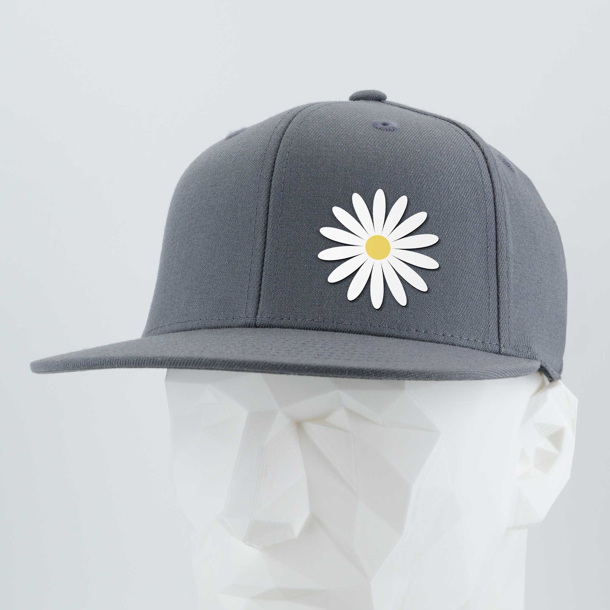 The Daisy (Silicone) - Flexfit® Flat Bill Premium Fitted Cap by Eternal Glyph features a white daisy with a yellow center on a gray cap, shown on a mannequin—an everyday hat symbolizing optimism.
