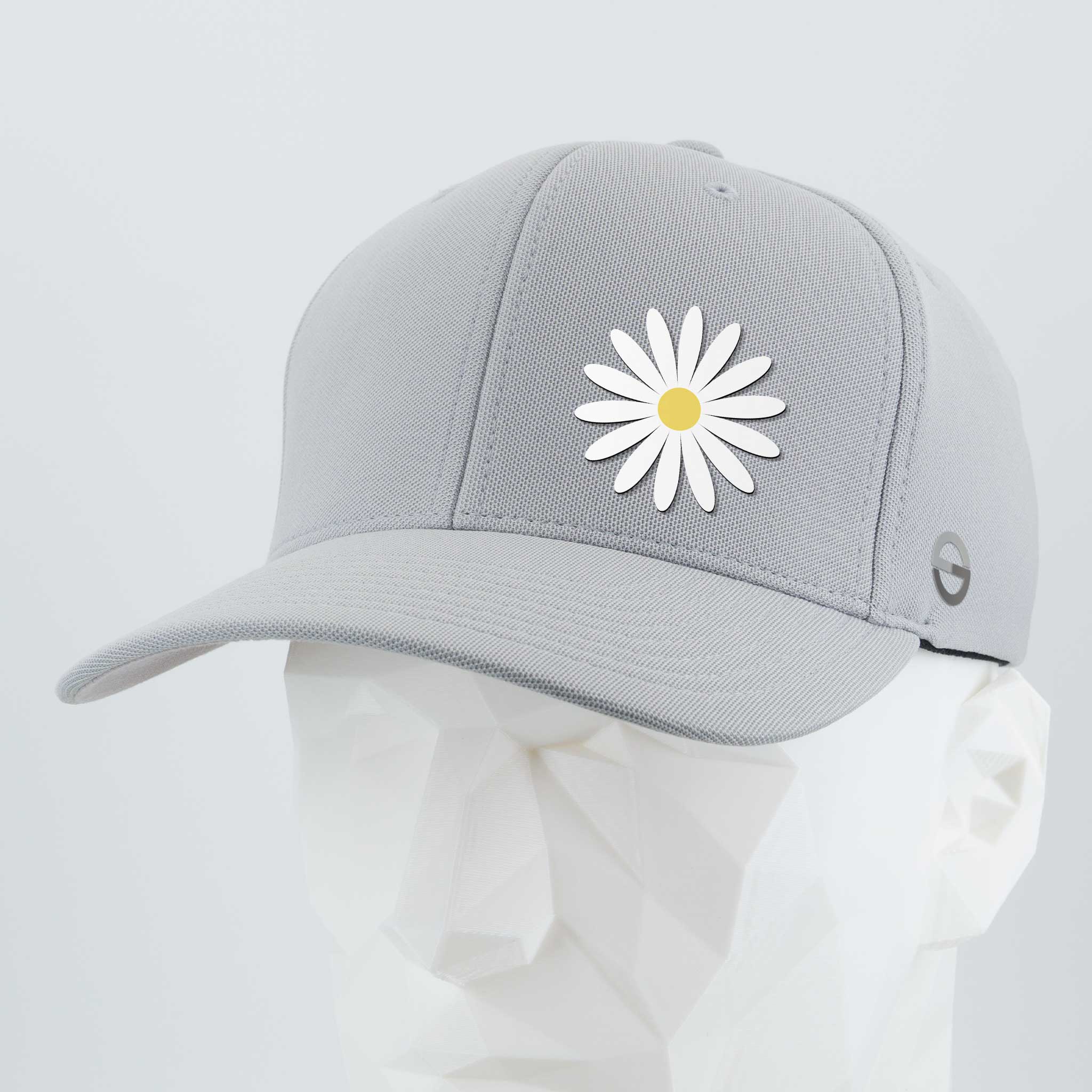 The Daisy - Flexfit® Cool & Dry Cap by Eternal Glyph is a light gray cap with a white daisy and yellow center, symbolizing optimism, shown on a white geometric mannequin head against a plain background.