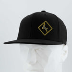The Eternal Glyph Deer Crossing Sign (Silicone) Flexfit® Flat Bill Premium Fitted Cap, in black with a yellow deer emblem, is shown on a white geometric mannequin against a light gray background.