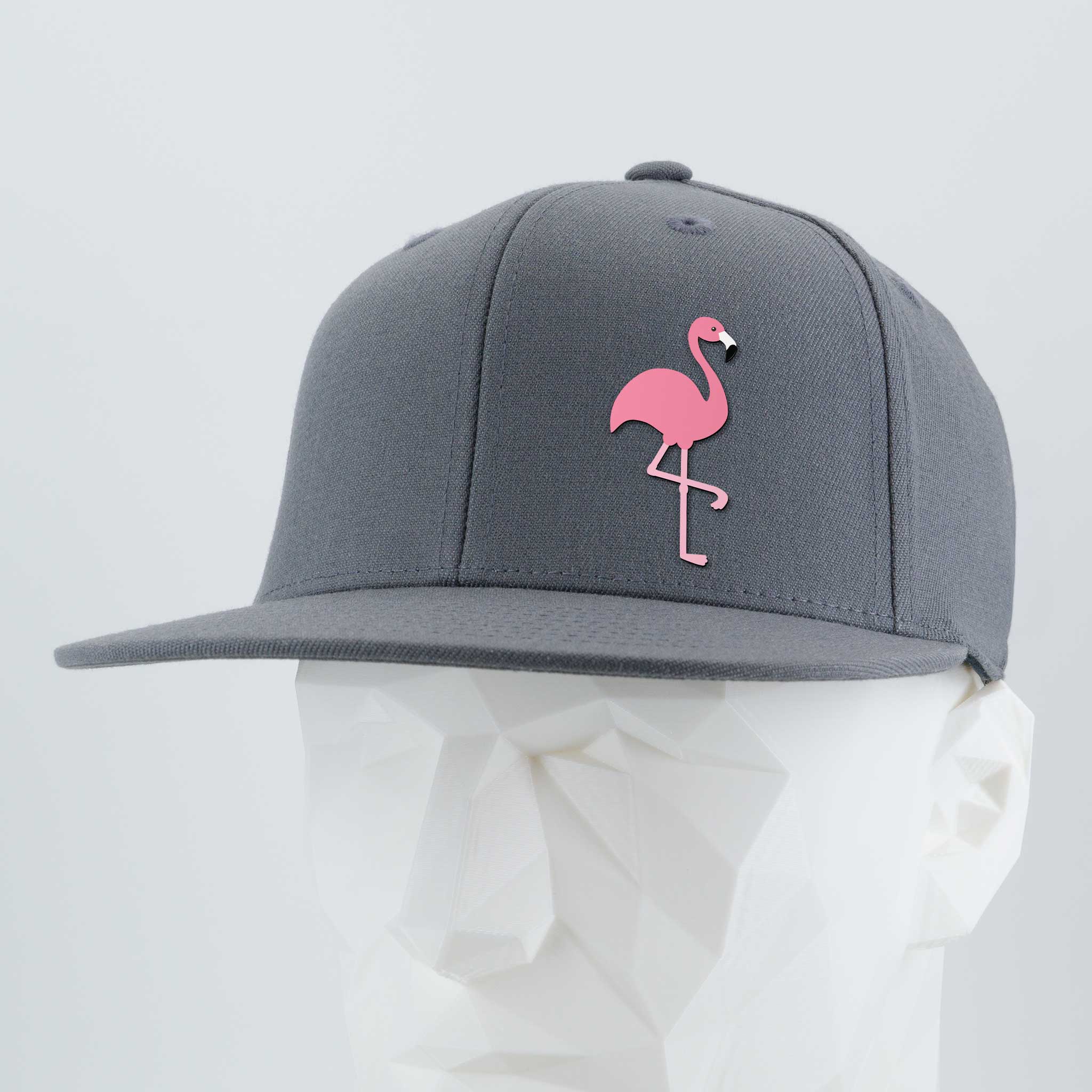 The Eternal Glyph Pink Flamingo (Silicone) Flexfit® Flat Bill Premium Fitted Cap is a gray snapback featuring a pink flamingo glyph on the front, shown on a white mannequin head against a light gray backdrop. Retro vacation vibes.