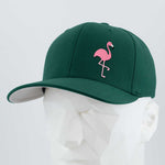 The Eternal Glyph Pink Flamingo (Silicone) Flexfit® Premium Wool Blend Cap features a dark green hue with a playful pink flamingo glyph, inspired by retro lawn decor and summer vibes, shown on a white geometric mannequin head.