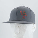 The Eternal Glyph Flexfit® Flat Bill Premium Fitted Cap in dark gray features a red outlined abstract Friendly Man Petroglyph (Silicone) on the front, inspired by Moab, Utah rock art, shown on a white mannequin against a light gray background.