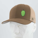 The Eternal Glyph Hop Cone (Silicone) Flexfit® Mesh Trucker Cap features a brown and beige design with a green hop cone symbol—ideal for beer lovers—shown here on a white geometric mannequin head.