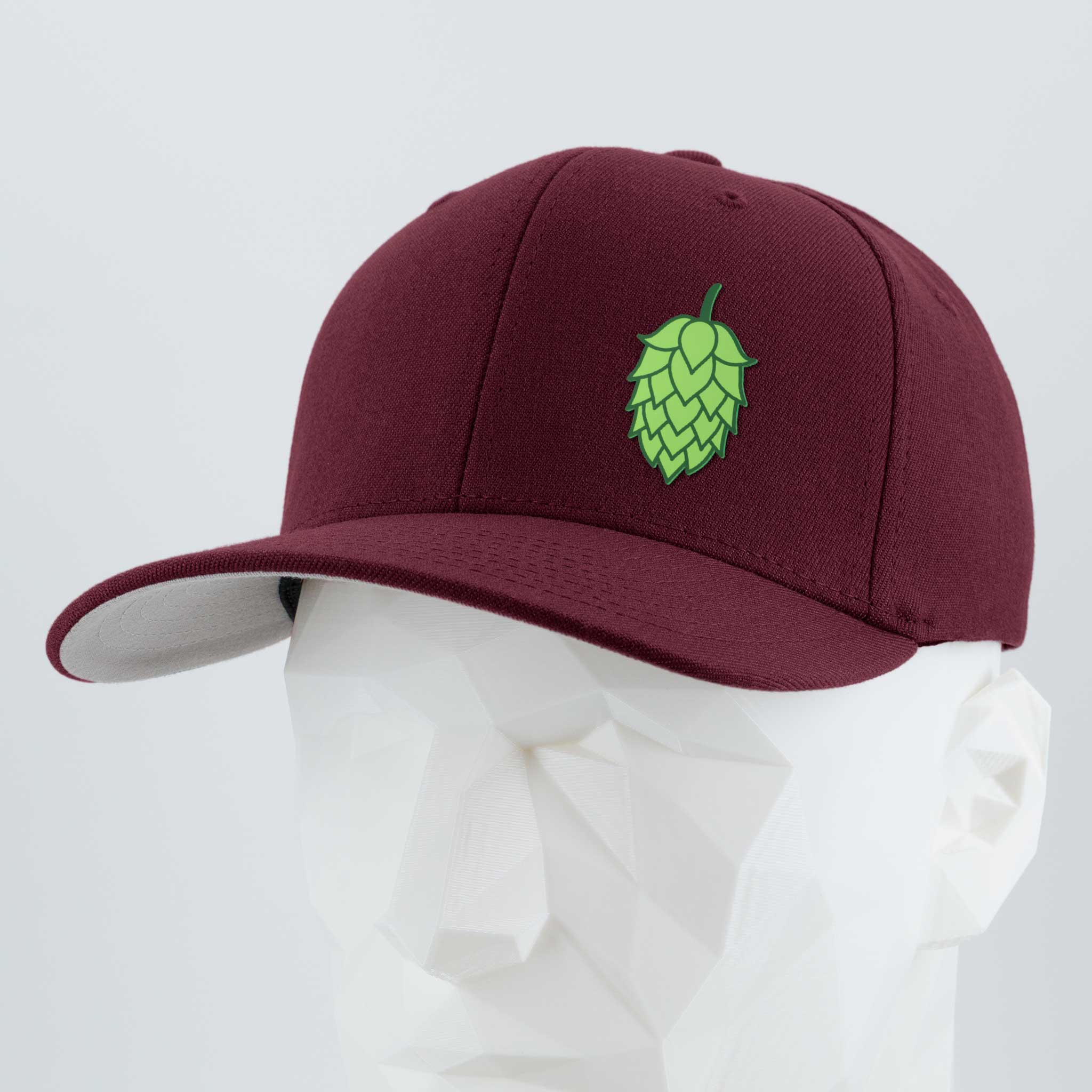 The Eternal Glyph Hop Cone (Silicone) Flexfit® Premium Wool Blend Cap is a maroon baseball hat with a green hop cone emblem, shown on a white geometric mannequin head against a plain backdrop—ideal for beer enthusiasts.