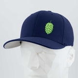 The Eternal Glyph Hop Cone (Silicone) Flexfit® Premium Wool Blend Cap in navy, featuring a hop cone emblem, is shown on a white geometric mannequin against a plain light background—ideal for beer enthusiasts.
