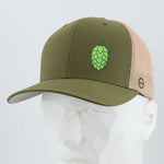 The Eternal Glyph Hop Cone (Silicone) - Flexfit® Mesh Trucker Cap in olive green and beige features a green hop cone on the front, shown on a faceted white mannequin head with a light gray background—ideal for beer lovers.