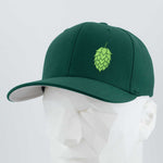 The Eternal Glyph Hop Cone (Silicone) Flexfit® Premium Wool Blend Cap features a dark green design with a light green hop cone emblem, ideal for beer lovers, shown on a white geometric mannequin against a plain backdrop.