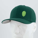 The Eternal Glyph Hop Cone (Silicone) Flexfit® Premium Wool Blend Cap features a dark green design with a light green hop cone emblem, ideal for beer lovers, shown on a white geometric mannequin against a plain backdrop.