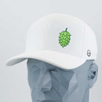The Eternal Glyph Hop Cone (Silicone) Flexfit® Cool & Dry Cap is a white hat with a bold green hop cone symbol on the front and a small circular logo on the side, shown on a gray geometric mannequin—ideal for craft brewing fans.