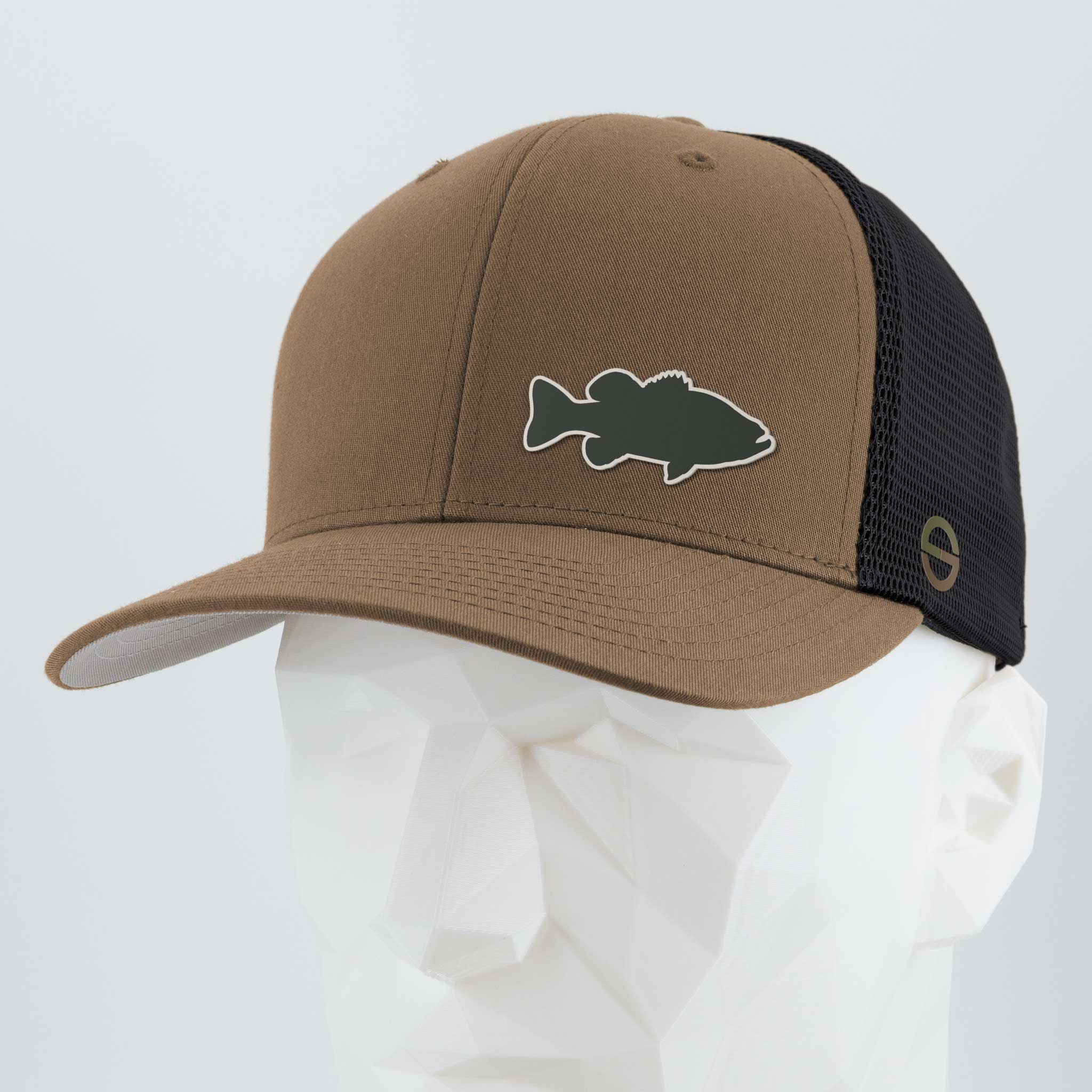 Coyote/Black Eternal Glyph Flexfit® Mesh Trucker Cap, featuring a large mouth bass fishing silicone patch on the front, shown on a white geometric mannequin head with a light gray backdrop.