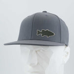 The Eternal Glyph Large Mouth Bass (Silicone) Flexfit® Flat Bill Premium Fitted Cap in gray features a black bass fishing silhouette patch on the front, shown on a white geometric mannequin head.