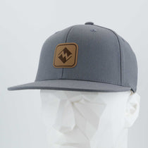 The Eternal Glyph Most Difficult Trail Sign (Leather) Flexfit® Flat Bill Cap features a gray snapback style with a geometric mountain logo patch, shown on a white mannequin head against a light background—perfect for outdoor adventures.