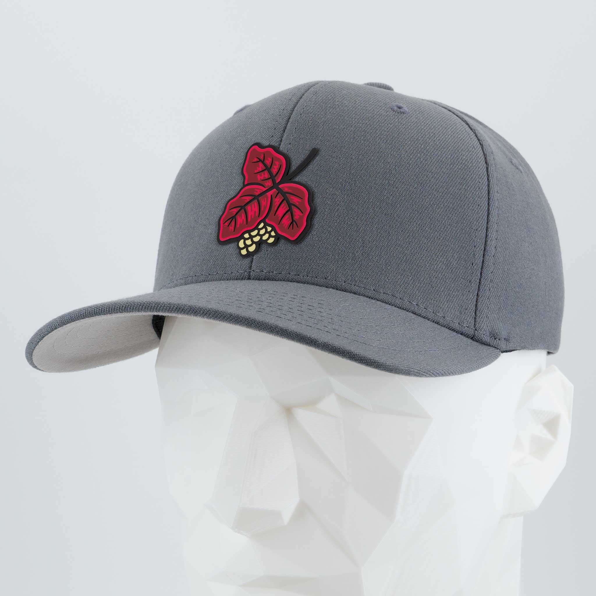 The Poison Oak (Double Layer Silicone) Flexfit® Premium Wool Blend Cap by Eternal Glyph features a red leaf and yellow grape patch, shown on a white geometric mannequin head against a plain background. Perfect for outdoor enthusiasts.