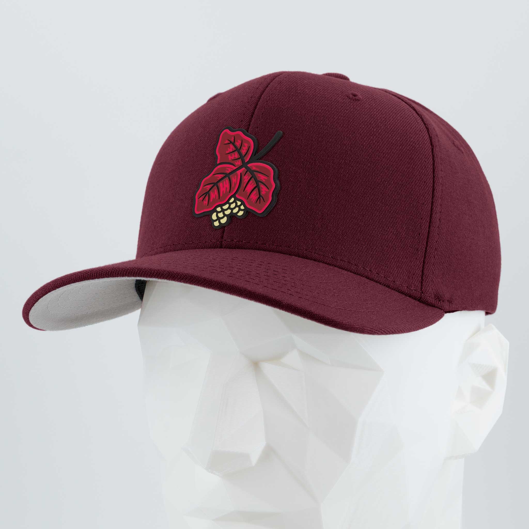 The Eternal Glyph Poison Oak (Double Layer Silicone) Flexfit® Premium Wool Blend Cap features a maroon design with a red leaf and yellow berries, inspired by poison oak, showcased on a white geometric mannequin head.