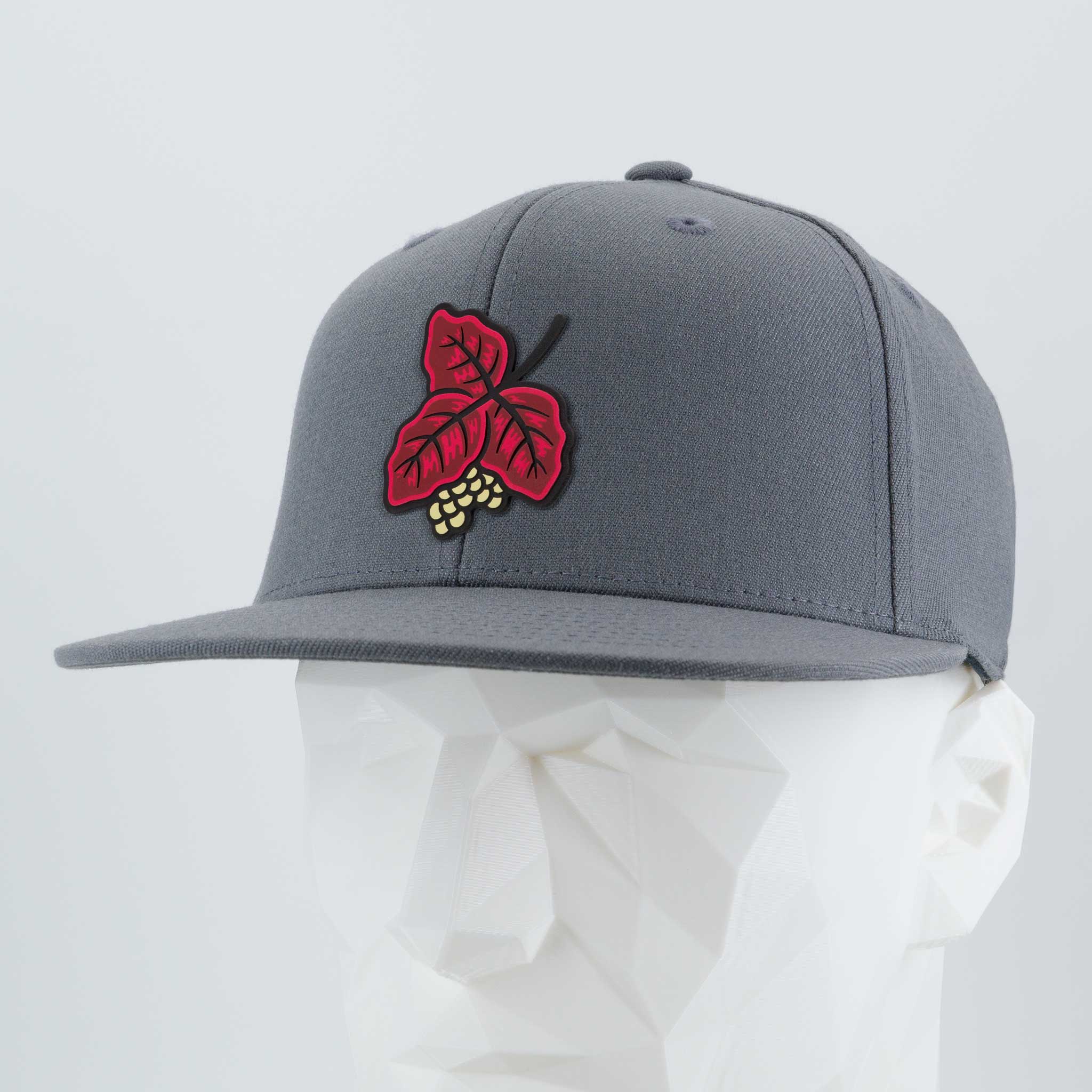 The Eternal Glyph Poison Oak (Double Layer Silicone) Flexfit® Flat Bill Premium Fitted Cap, in gray with a red leaf and yellow berry patch, is shown on a white faceted mannequin head against a plain light backdrop.