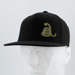 The Eternal Glyph Coiled Rattlesnake Silhouette Flexfit® Flat Bill Premium Fitted Cap in black features a yellow Gadsden-inspired emblem, shown on a white faceted mannequin against a light gray background.