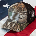 The Eternal Glyph American Flag Flexfit® Mesh Trucker Cap features Realtree® Edge camo, a double-layer silicone American flag patch, mesh backing, and Realtree® logos on front and side.